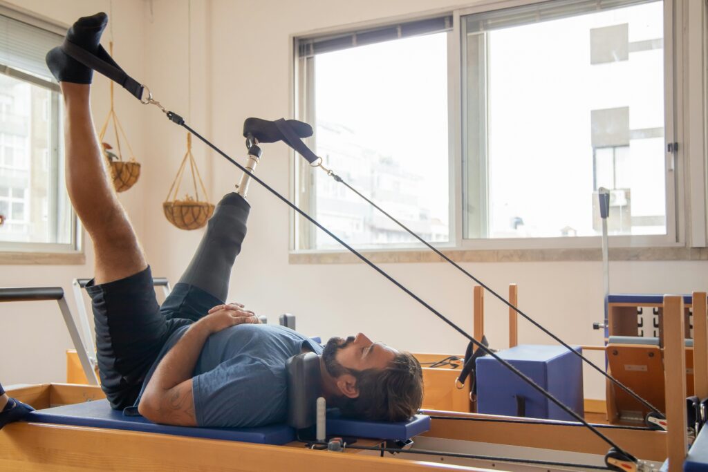 Man with prosthetic leg performing pilates therapy on reformer machine